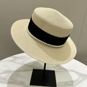 Detail of elegant straw boater hat featuring pearl inlay and a black ribbon on a stand