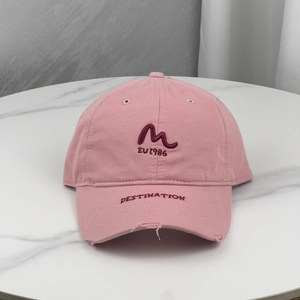 Pink distressed baseball cap with M embroidery on a marble surface in a top-down view