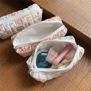 Detail of three floral quilted cotton cosmetic bags on a wooden table for makeup storage