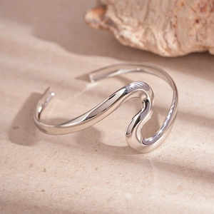 Detail of a wavy silver open cuff bracelet with polished finish on a sandy texture