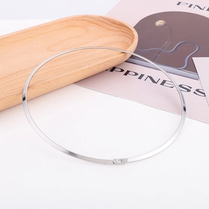 Close-up of minimalist silver stainless steel necklace on a wooden tray with a polished finish
