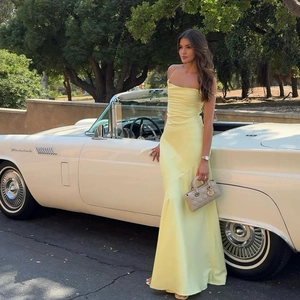 Robe longue en satin jaune pâle avec dos nu, présentée près d'une voiture de collection
