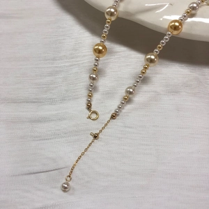 Close-up of multicolored pearls with gold-plated clasp and adjustable chain on white cloth