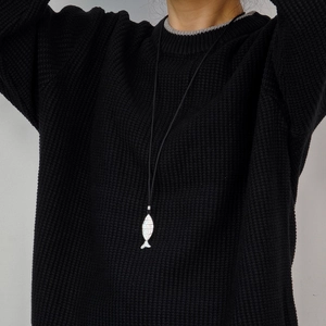 Minimalist fish pendant necklace with black cord shown on a black knitted sweater