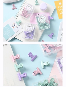 Détail macro de pinces à reliure pastel en métal dans une boîte de bureau élégante