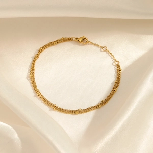 Elegant gold plated double layer beaded bracelet on white silk fabric background