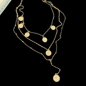 Macro detail of gold layered coin necklace with portrait pendants and long chain tassel