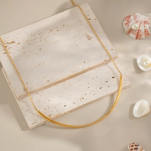 Minimalist 18K gold crescent necklace on beige travertine stone with seashells