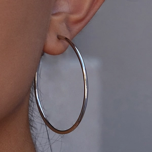 Minimalist large silver stainless steel hoop earrings worn on ear with polished finish