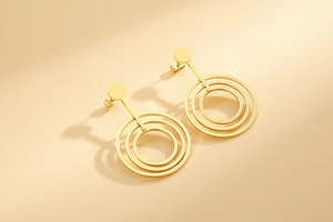 Detail of rose gold geometric dangle earrings with concentric circles on beige background