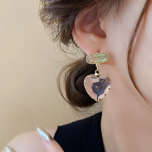 Nahaufnahme von Goldohrringen mit grünem Rechteck und rosa Herz-Edelstein an einem Model