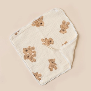 Detailed view of baby cotton bib with brown teddy bear print and white pom-pom trim