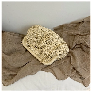 Top-down view of a beige straw woven shoulder bag with a gold chain on brown fabric