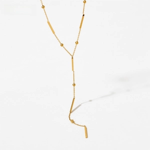 Detail view of a gold Y-shaped necklace with geometric beads and bar pendants on white background