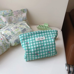 Flat lay of cotton cosmetic bags with green plaid and floral prints and zipper closure