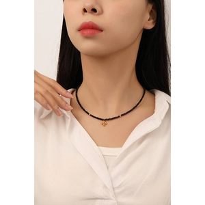 Minimalist black beaded choker necklace with a gold cross flower pendant on a model