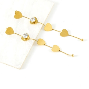 Detail of long gold heart drop earrings with zircon stone on white marble background