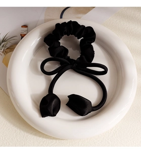 Close-up of black satin scrunchie with bow and tulip ribbon in a ceramic plate