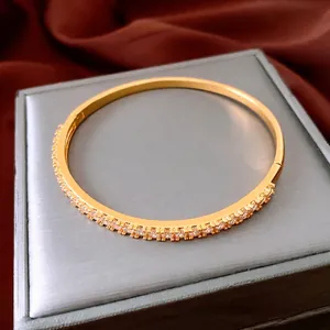 24K gold plated bangle with white zircon pave setting and hinge clasp on satin background