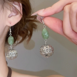 Détail des boucles d'oreilles boules argentées ajourées avec perles vertes sur modèle