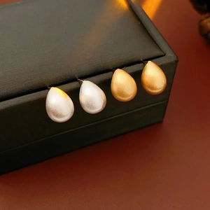 Close-up of gold and silver teardrop earrings with brushed texture on a jewelry box