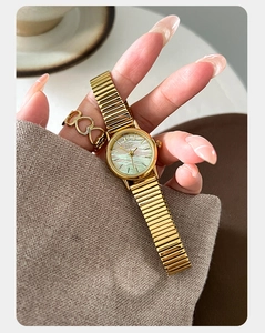 Close-up of golden ladies watch featuring iridescent mother of pearl dial and heart ring