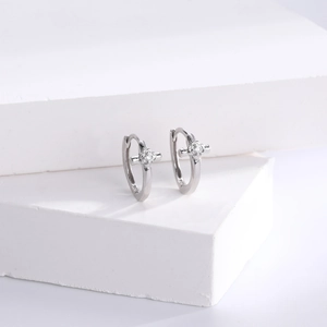 Macro detail of silver cross hoop earrings featuring sparkling cubic zirconia on a white stone