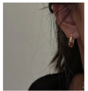 Close-up of polished gold U-shaped minimalist sterling silver earring worn on the ear