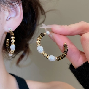 Dettaglio di orecchini a C con perle occhio di tigre, perle bianche e accenti dorati