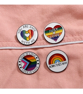 Detail of four rainbow enamel pins with inclusive slogans on pink denim fabric