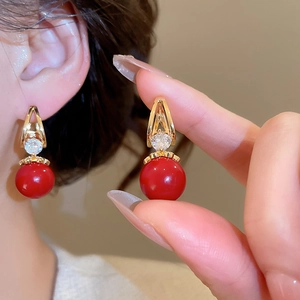 Détail de boucles d'oreilles perles rouges et zircons blancs portées pour voir la taille