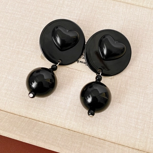 Detail of black acrylic bead earrings with silver connectors on beige fabric backdrop