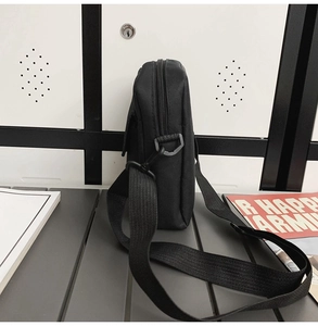 Side view of black nylon messenger bag with woven strap and buckle on grey surface