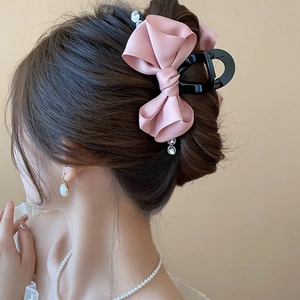 Detail of pink satin bow hair claw with pearl pendant on model’s elegant hairstyle