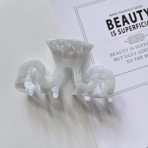 Gros plan d'une pince à cheveux en acétate marbré blanc au design ondulé et évidé
