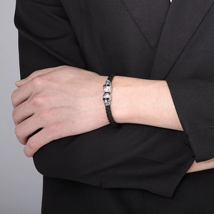 Detail of woven black leather bracelet with double silver skull heads on model wrist