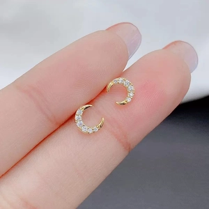 Delicate gold crescent moon stud earrings with white zircon crystals held by fingers