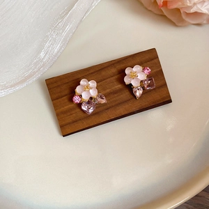 Detail of pink floral stud earrings with crystals on wood and white satin fabric