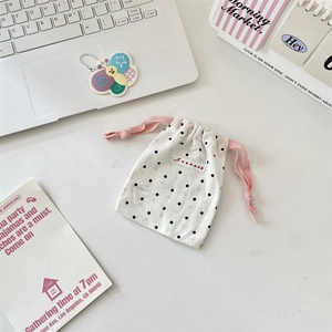 Close-up of white polka dot drawstring pouch with a pink cord and woven logo label