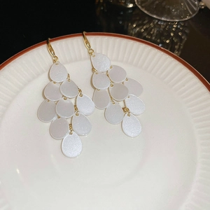 Macro detail of Bohemian white layered teardrop earrings with gold hooks on a ceramic plate