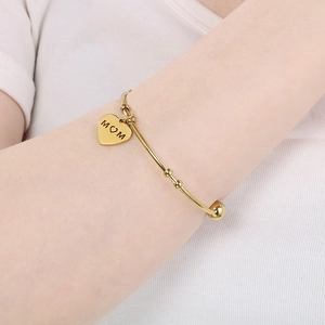 Close-up of gold MOM heart pendant bracelet worn by a model in a minimalist style
