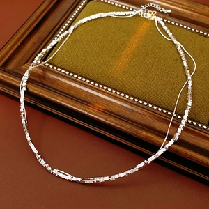 Detailed view of silver double-layered chain necklace featuring square beads on green velvet