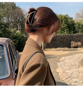 Detail of a large golden metal hair claw clip with white pearls worn on a bun hairstyle