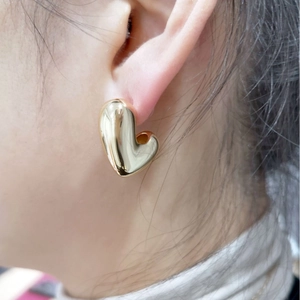 Minimalist large golden heart-shaped stud earrings with polished mirror finish on model