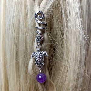 Close-up of a silver spiral hair ring with a turtle charm and purple amethyst bead