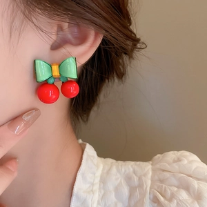 Gros plan de boucles d'oreilles cerises et nœuds en résine sur l'oreille