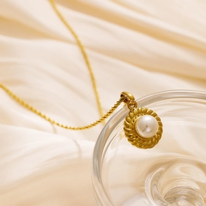 Collar de titanio bañado en oro de 18k con colgante de perla vintage sobre fondo de satén