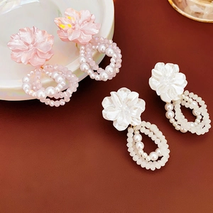 Detail of pink and white floral earrings with pearl beads on a rustic surface