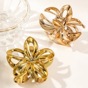 Close-up of dual gold metal frangipani flower hair claws on a clean white surface