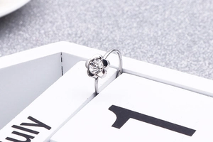 Close-up of a silver flower ring with a sparkling zircon stone on a grey surface